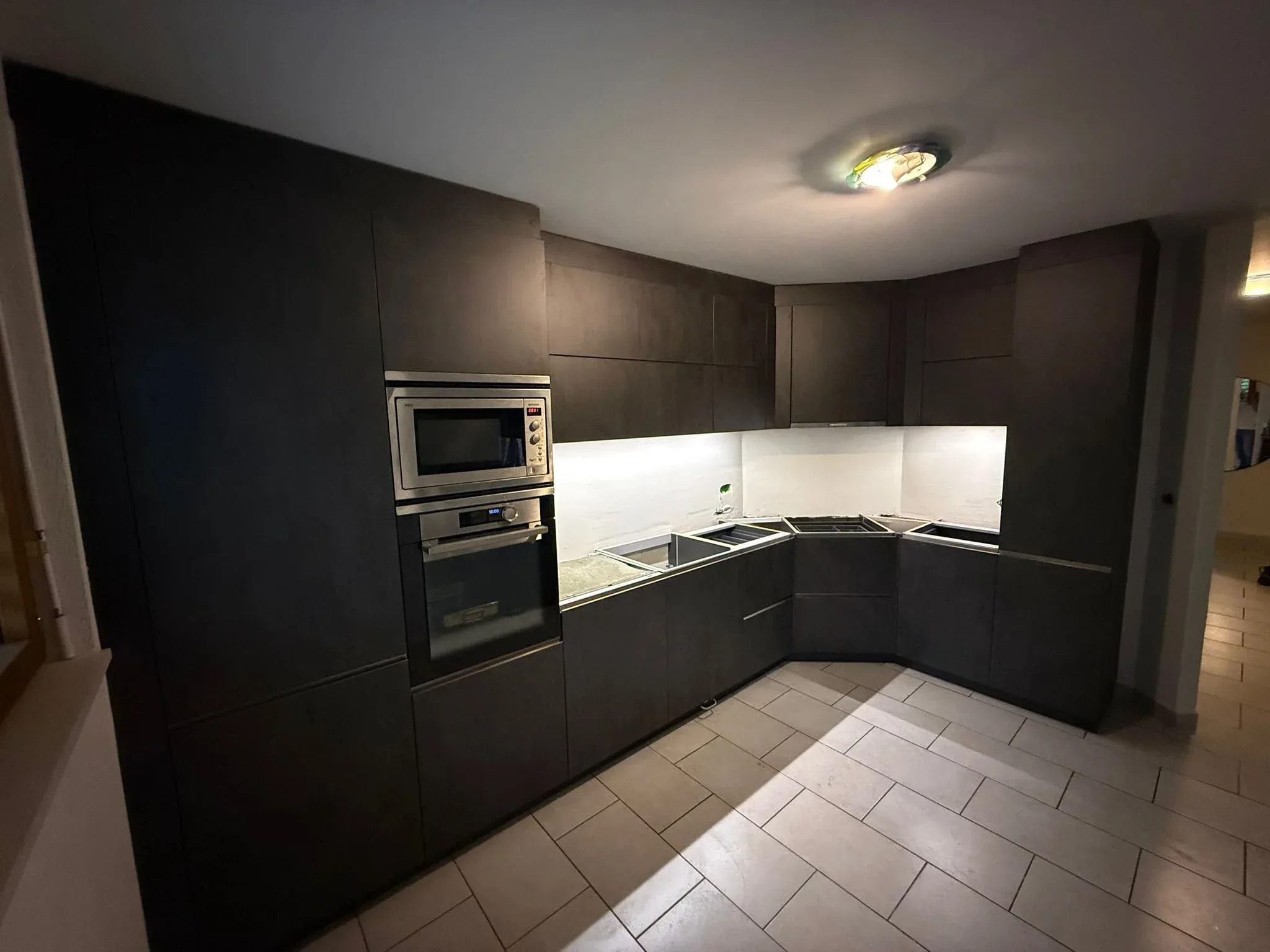 Cuisine en L aux façades anthracite mat, four et micro-ondes encastrés, en cours de pose