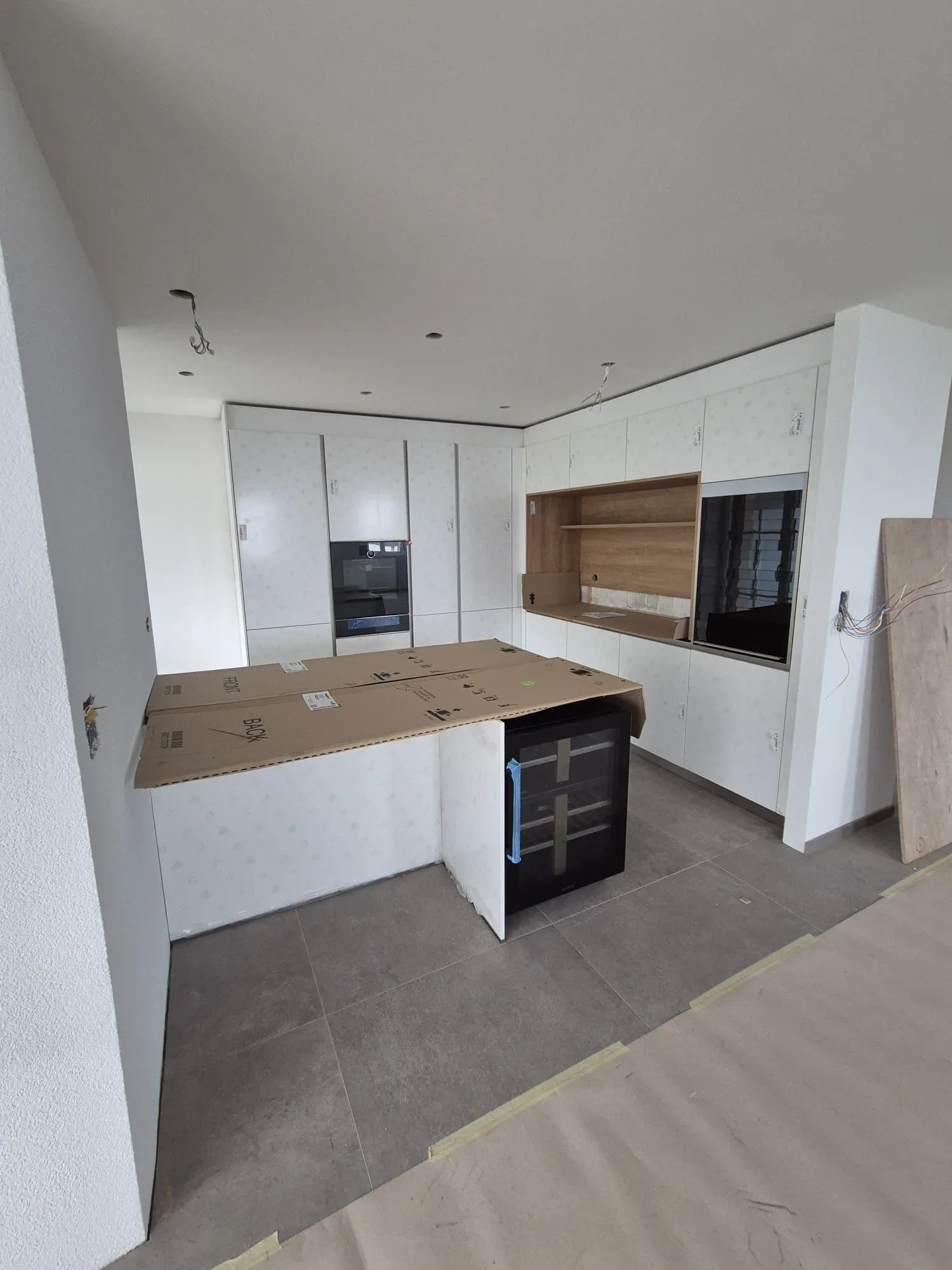 Cuisine blanche mate en U avec îlot, appareils encore protégés, sur chantier neuf